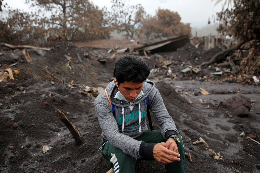 A resident sits on the rubble as people continue to search for remains of victims after the eruption of the Fuego volcano at San Miguel Los Lotes in Escuintla, Guatemala, June 17, 2018. REUTERS/Luis Echeverria 