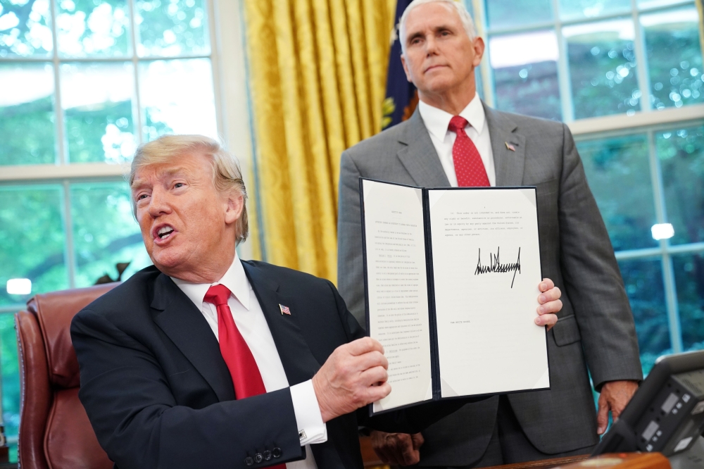 Watched by Vice President Mike Pence, US President Donald Trump shows an executive order on immigration which he just signed in the Oval Office of the White House on June 20, 2018 in Washington, DC.   AFP / Mandel Ngan
