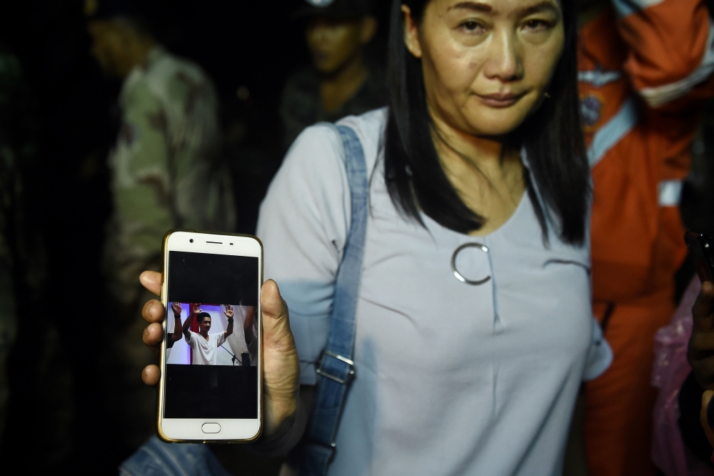 A relative shows the photograph of missing Adorn Sanorn, 14, as family members keep vigil near Tham Luang cave at the Khun Nam Nang Non Forest Park in Chiang Rai on June 26, 2018 while rescue personnel conduct operation for a missing children's football t