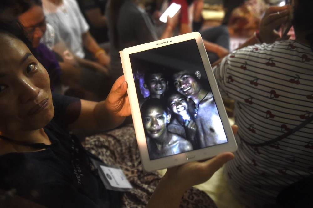 A family member shows a picture of four of the twelve missing boys near the Tham Luang cave at the Khun Nam Nang Non Forest Park in Mae Sai on July 2, 2018.  AFP / Lillian Suwanrumpha