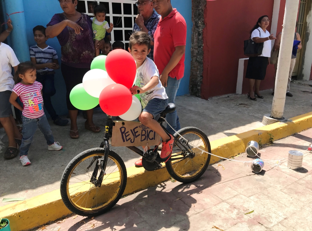 A child rides a bike adorned with balloons and a sign reading 