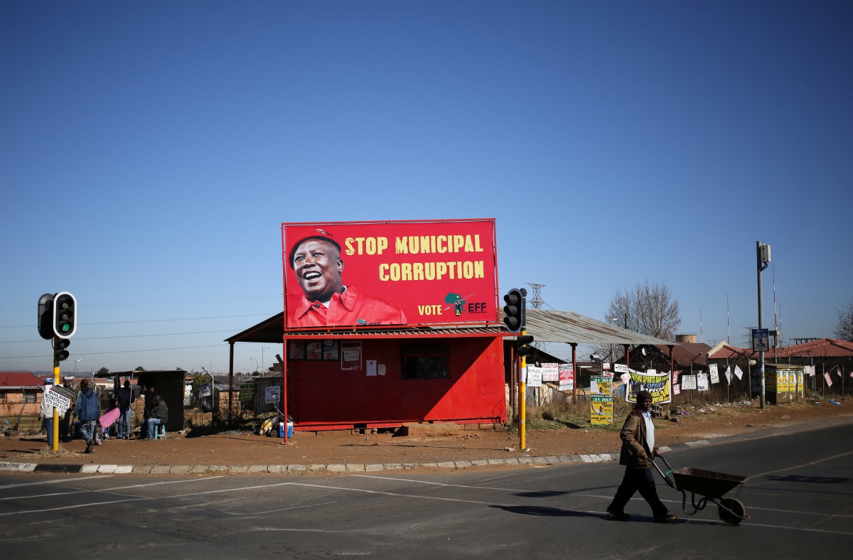 FILE PHOTO: A man pushes a wheelbarrow past a billboard of the Economic Freedom Fighters which is led by Julius Malema in Soweto,  South Africa,  August 5, 2016. Reuters/Siphiwe Sibeko