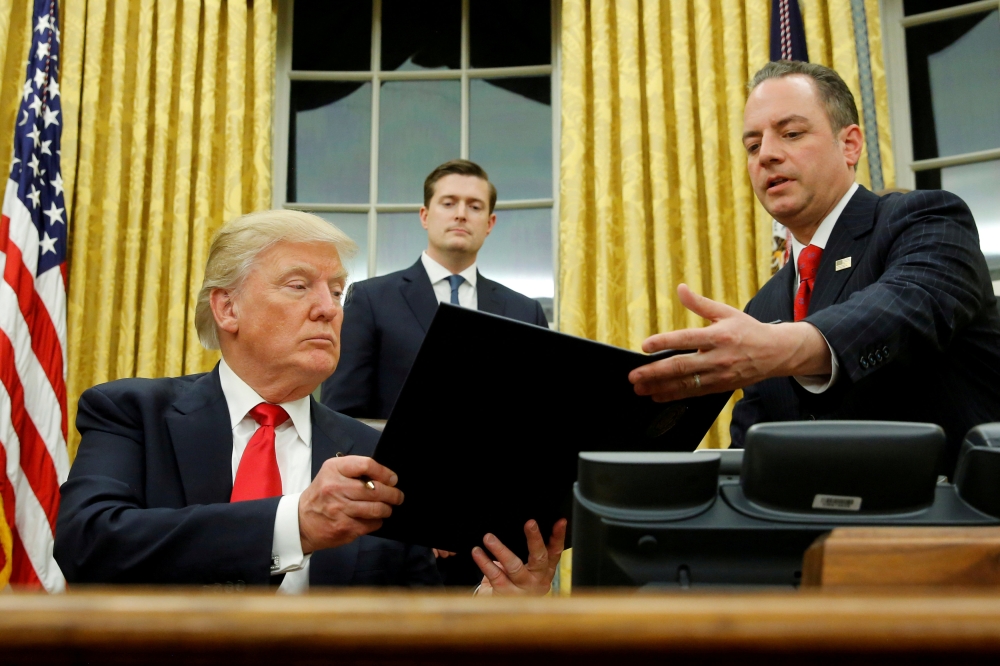 FILE PHOTO: US President Donald Trump hands Chief of Staff Reince Priebus (R) an executive order that directs agencies to ease the burden of Obamacare, after signing it in the Oval Office in Washington, DC, U.S. January 20, 2017. Also pictured is White Ho