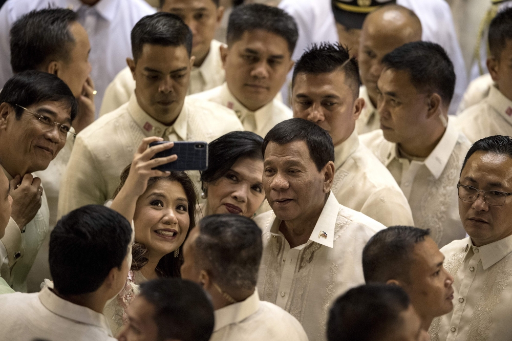 Philippine President Rodrigo Duterte poses for a selfie while surrounded by supporters and lawmakers after delivering his state of the nation address at Congress in Manila on July 23, 2018. (AFP / NOEL CELIS)