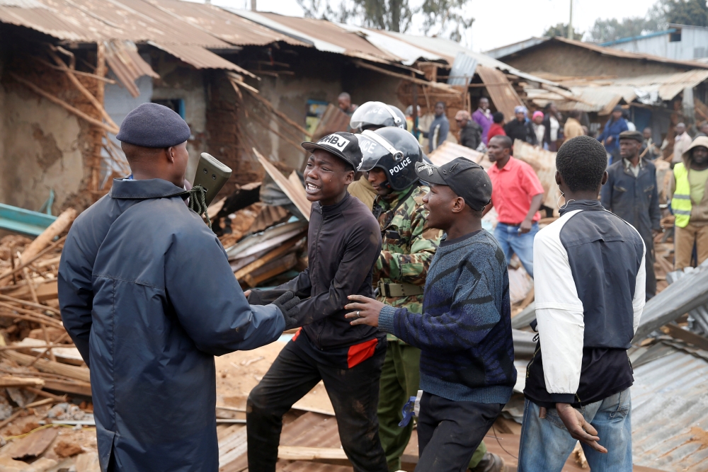 A youth is escorted by Kenyan police officers as dozens of houses are being demolished to make way for a new road in the Kibera slum in Nairobi, Kenya, July 23, 2018. Reuters/Baz Ratner