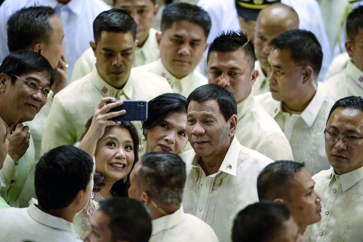 Philippine President Rodrigo Duterte poses for a selfie while surrounded by supporters and lawmakers after delivering his state of the nation address at Congress in Manila on July 23, 2018. / AFP / Noel Celis