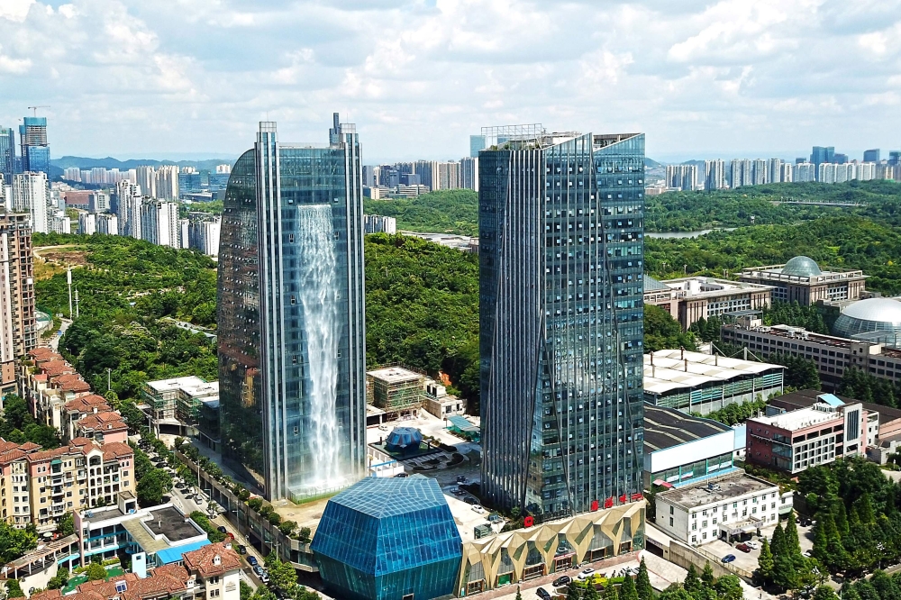 This photo taken on July 20, 2018 shows a 108-meter-high (350 feet) artificial waterfall on the facade of the Liebian International Building (L) in Guiyang in China's southwestern Guizhou province.  AFP
