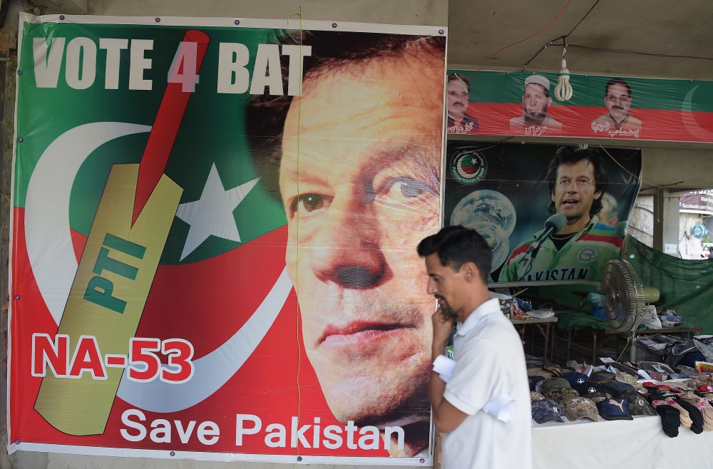 A man walks past a poster of Pakistan's cricketer-turned politician Imran Khan, and head of the Pakistan Tehreek-e-Insaf (Movement for Justice) party, at a market in Islamabad on July 27, 2018. (AFP / AAMIR QURESHI)