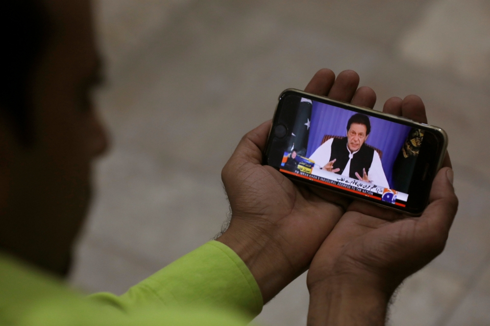 A journalist poses with a cell phone displaying Imran Khan, Prime Minister of Pakistan, speaking to the nation in his first televised address, in Karachi, Pakistan August 19, 2018. (REUTERS/Akhtar Soomro)