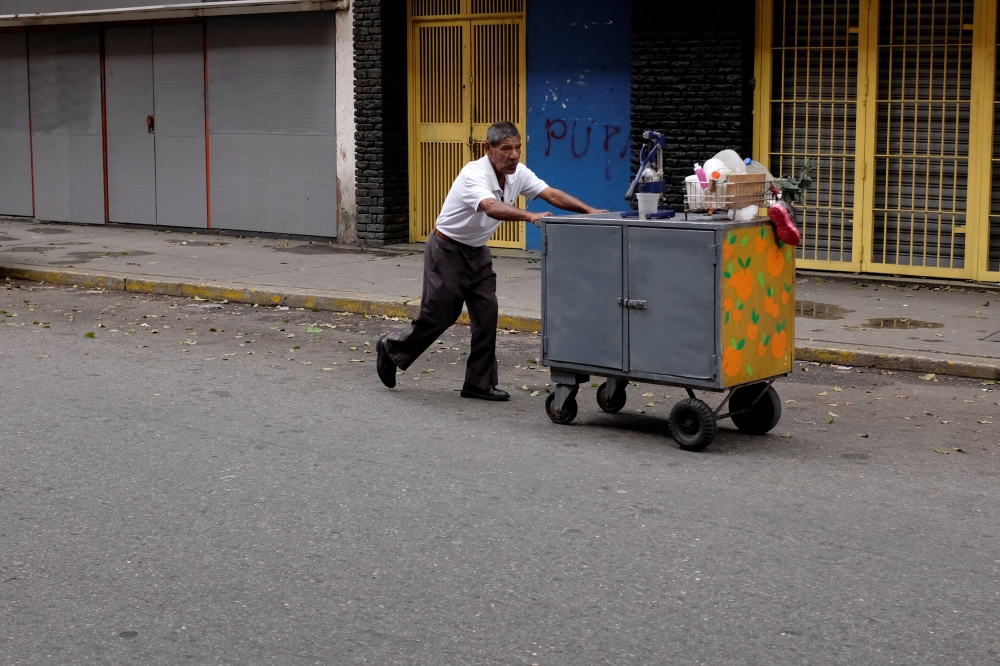 A man pushes a cart in front of closed stores at a commercial area in downtown Caracas, Venezuela August 21, 2018. REUTERS/Marco Bello
