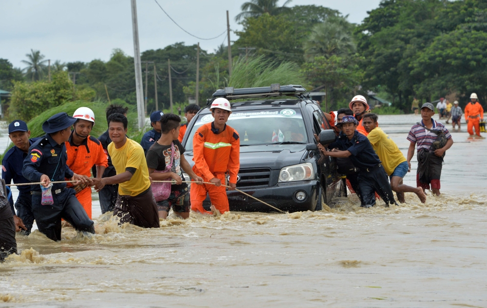 Residents negotiate a flooded road after rampaging waters from a dam spillway submerged villages in Bago region, central Myanmar on August 29, 2018. AFP / Thet AUNG