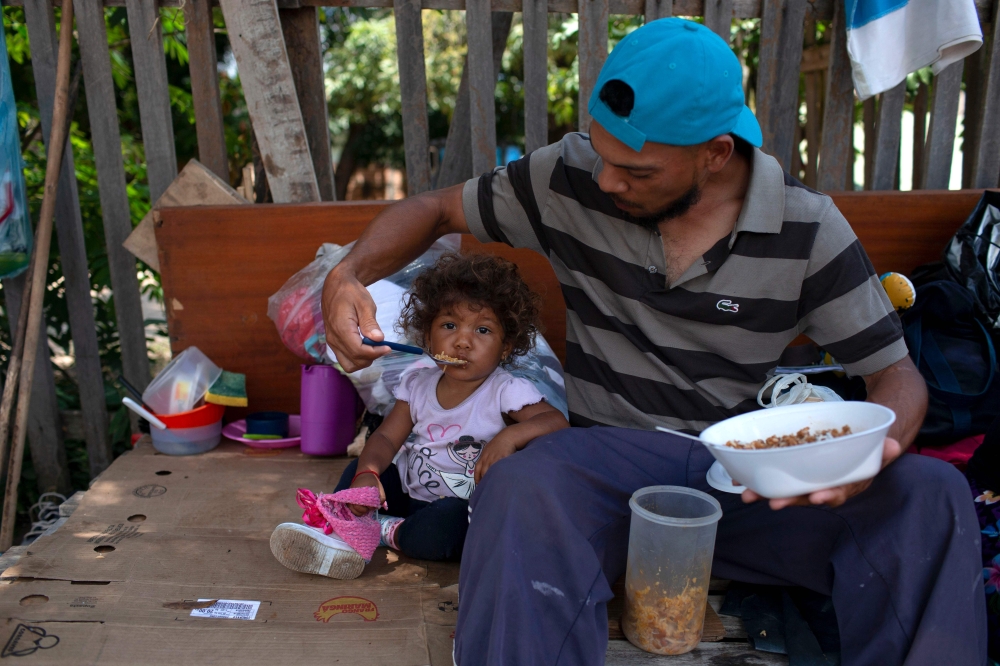 FILE PHOTO: In this file photo taken on August 23, 2018 a Venezuelan man and his daughter eat a meal on the side of a road in Boa Vista, Roraima state, Brazil. / AFP / Mauro Pimentel