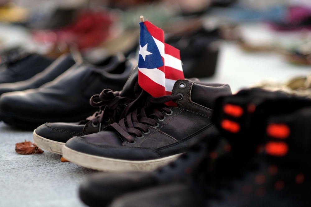 :(FILES) In this file photo taken on June 1, 2018 a view of a Puerto Rican flag placed on a pair of shoes among hundreds displayed in memory of those killed by Hurricane Maria in front of the Puerto Rican Capitol, in San Juan.  AFP / Ricardo ARDUENGO
