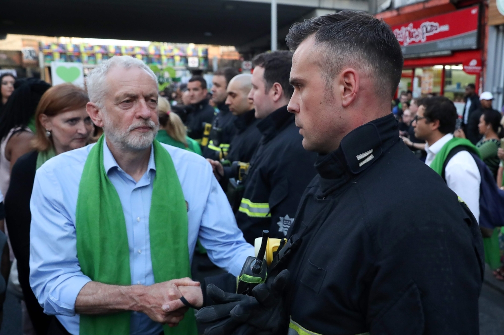 Jeremy Corbyn shakes hands with a fire-fighter lining the street as members of the public take part in a silent march on the first anniversary of the Grenfell fire on June 14, 2018. AFP / Daniel Leal-Olivas
