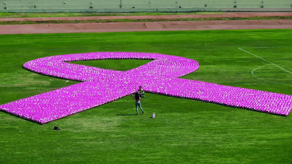 In this file photo taken on October 8, 2017 people gather around a pink ribbon, made up of eight thousand pink footballs, during an event to raise awarness on breast cancer at the Sport City Stadium in Beirut.  AFP / Anwar Amro