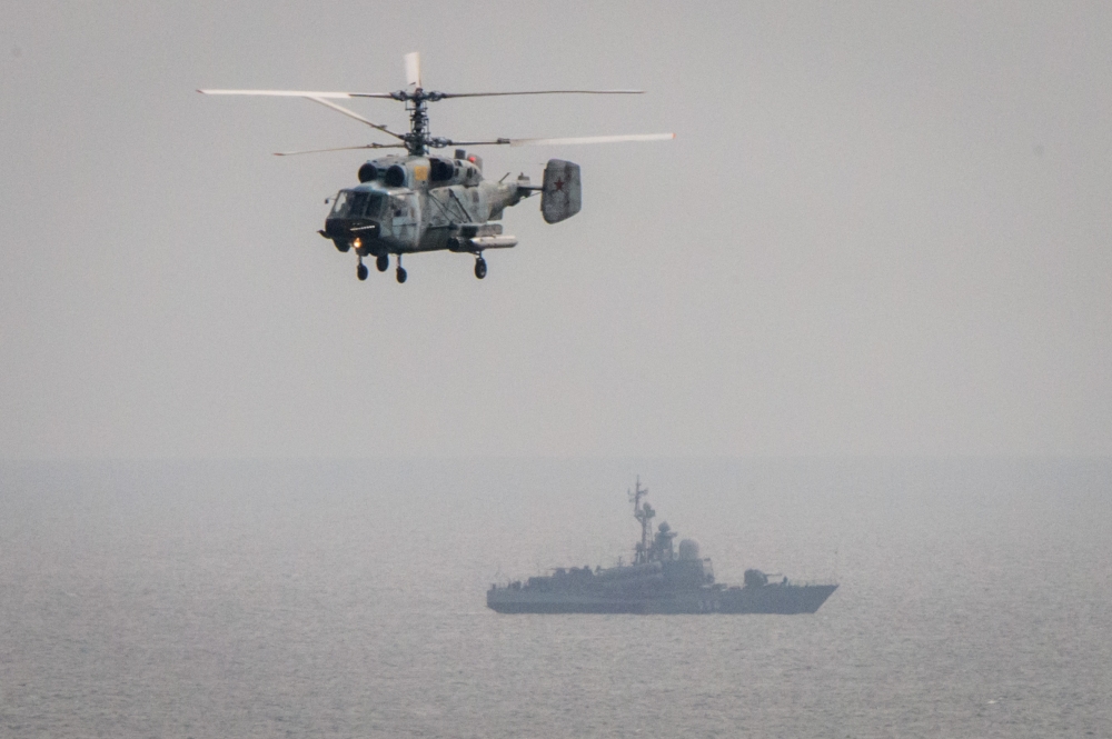 A military helicopter flies over a Russian battleship during the Vostok-2018 (East-2018) military drills at Klerka training ground on the Sea of Japan coast, outside the town of Slavyanka, some 100km south of Vladivostok, on September 15, 2018. / AFP / Ml