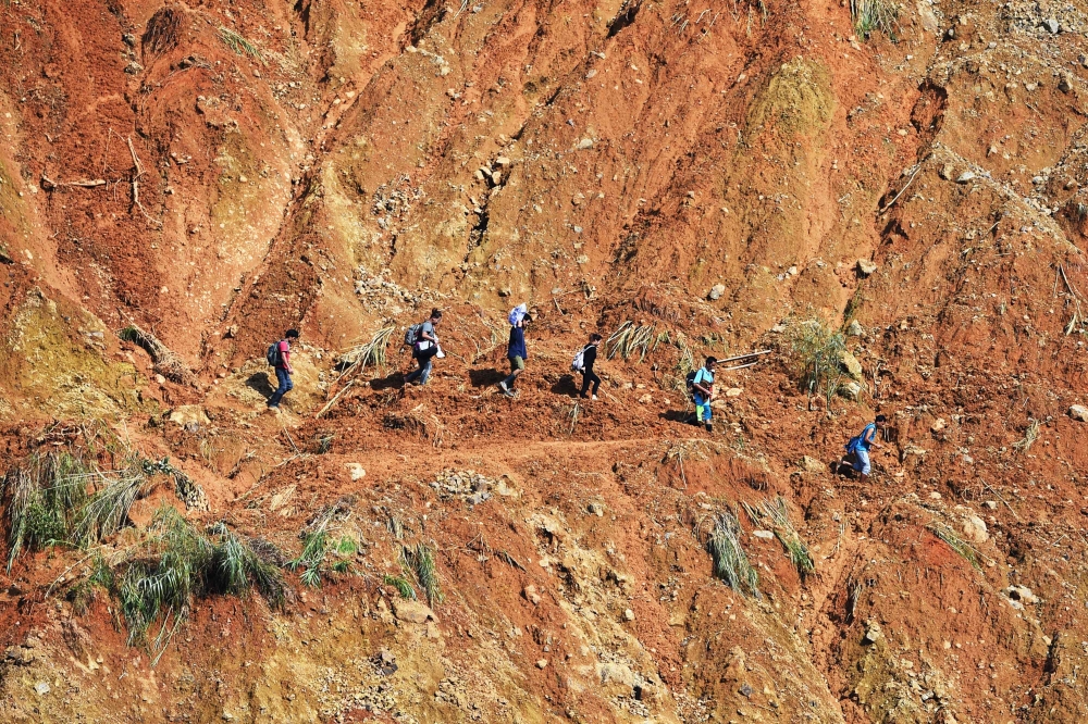 Residents walk with their belongings along a path at the site of a landslide, triggered by heavy rains during Typhoon Mangkhut, in Itogon, Benguet province on September 18, 2018.  AFP / TED ALJIBE