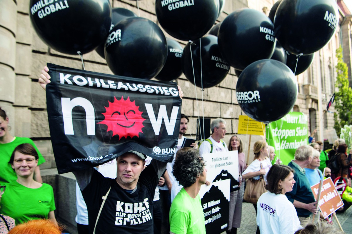 Environmental activists hold black balloons, posters and banners, reading for example 