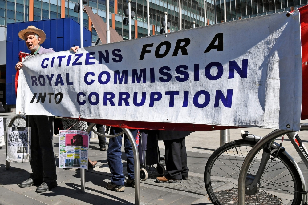 People hold a banner outside the Banking Royal Commission being held in Melbourne on September 26, 2018. / AFP / William WEST