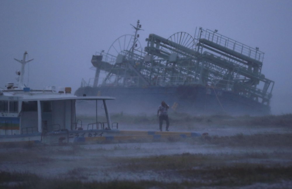 A person reacts to the weather as ship washed ashore caused by Typhoon Trami is seen at a port in Yonabaru, on the southern island of Okinawa, Japan, in this photo taken by Kyodo September 29, 2018. Kyodo via REUTERS