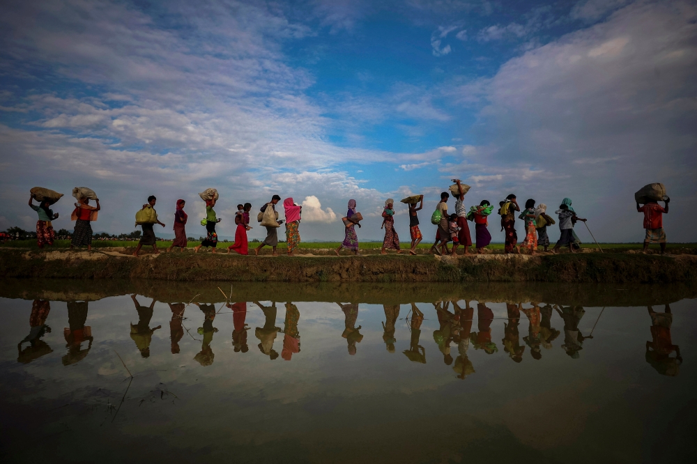 FILE PHOTO: Rohingya refugees are reflected in rainwater along an embankment next to paddy fields after fleeing from Myanmar into Palang Khali, near Cox's Bazar, Bangladesh November 2, 2017. REUTERS/Hannah McKay