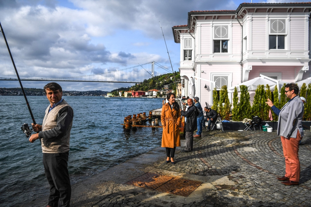 A fisherman watched by bystanders as he works beside waterside mansions on the Bosphorus River coast on the Asian side of Istanbul.  AFP / OZAN KOSE
