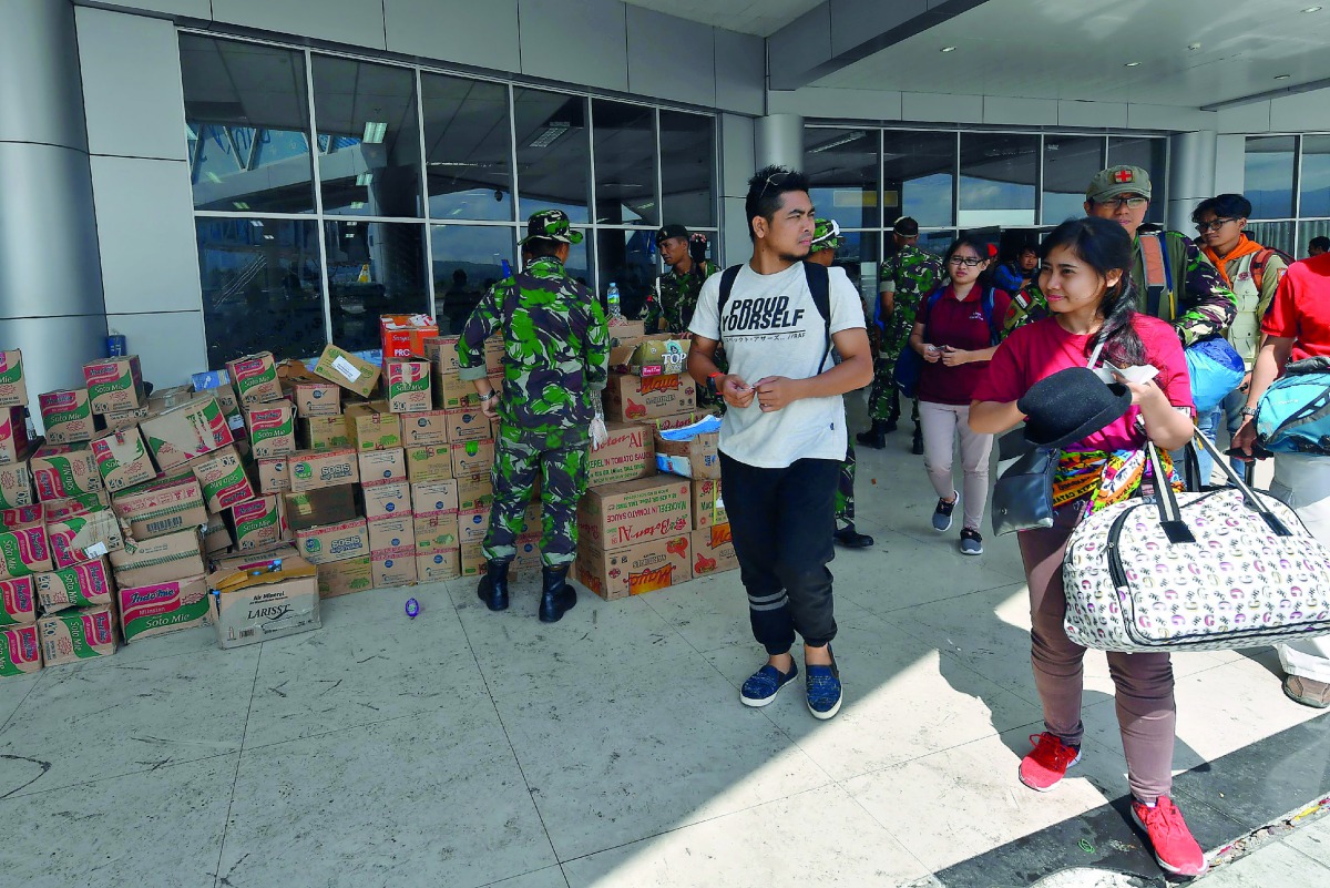 Passengers boarding a commercial flight walk past packages of aid at the Mutiara Sis Al Jufri airport in Palu on October 10, 2018, days after the airport reopened following the September 28 earthquake and tsunami.  AFP / Adek Berry


