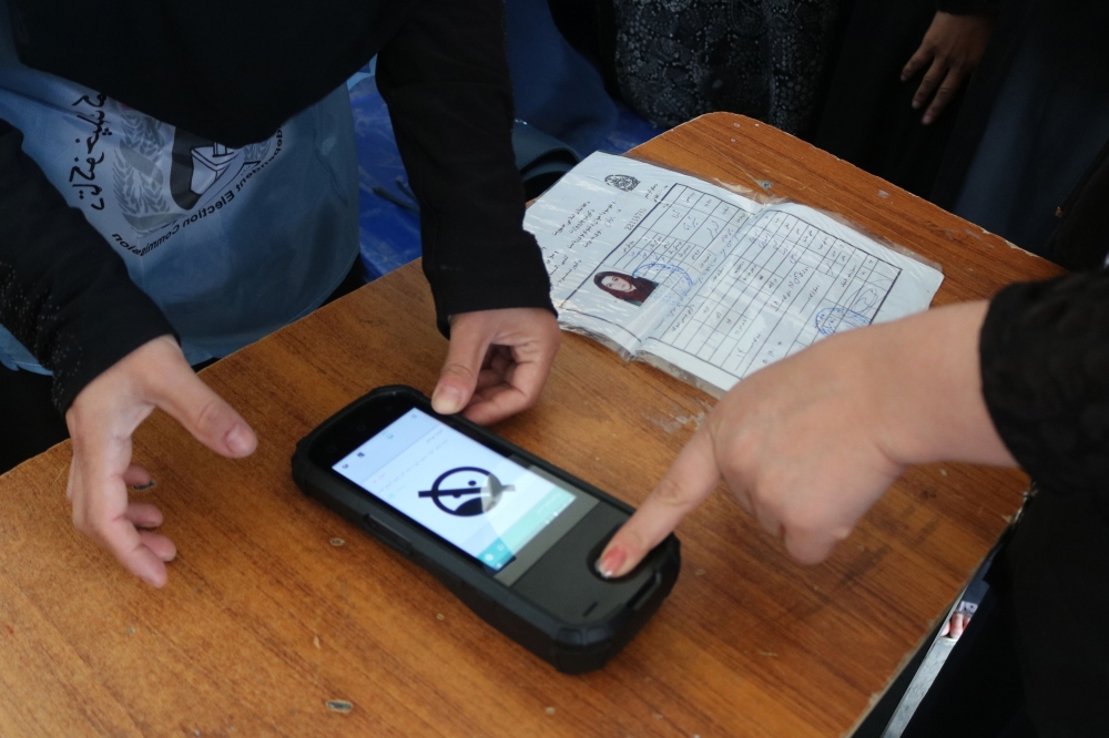  An Afghan Independent Election Commission (IEC) official (L) scans a voter's finger with a biometric device at a polling centre for the country's legislative election in Parwan province on October 20, 2018. / AFP / ABDUL SHAHMIM TANHA 