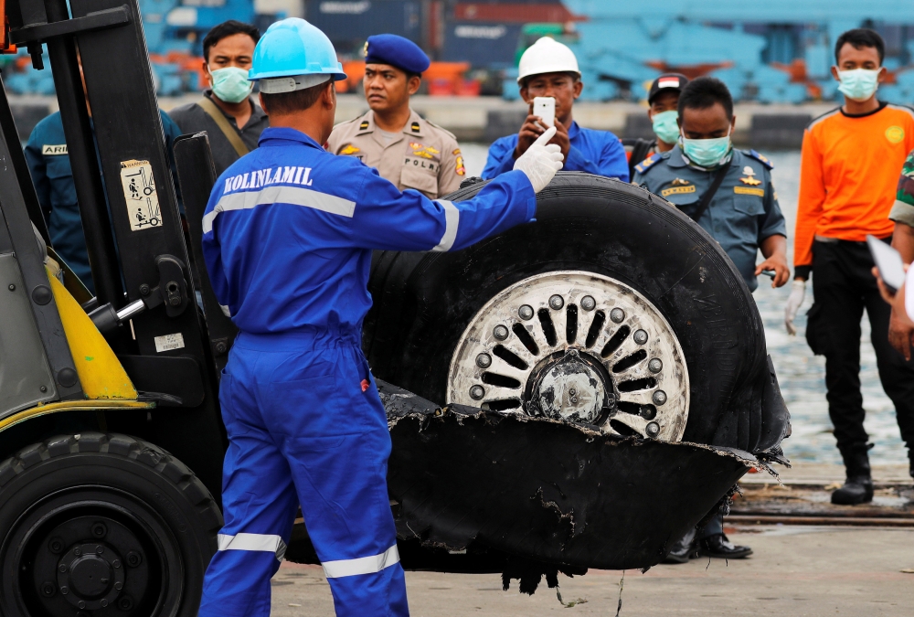 A worker assists his colleague during the lift up of a damaged tyre from the Lion Air flight JT610 jet, at Tanjung Priok port in Jakarta, Indonesia, November 5, 2018. REUTERS/Beawiharta