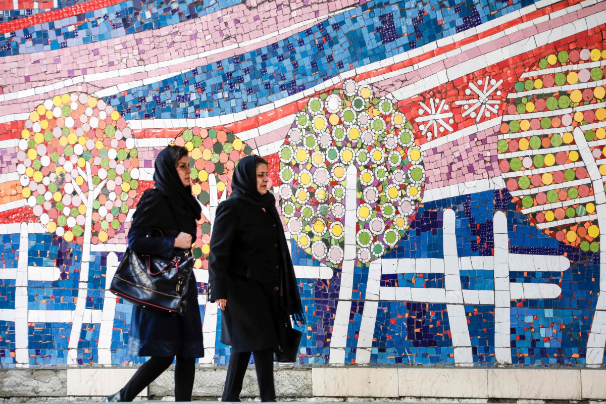 Two Iranian women walk along a street past a mosaic mural on Jaunary 14, 2017. AFP/Atta Kenare