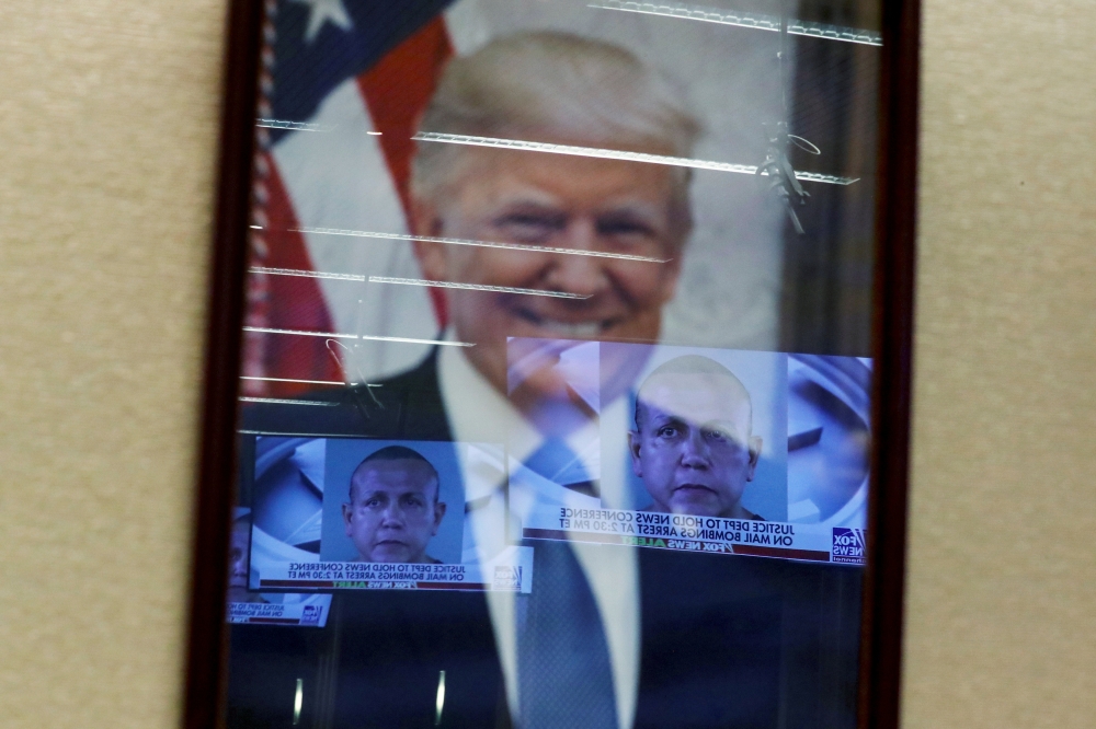 :FILE PHOTO: Televised pictures of parcel bombs suspect Cesar Sayoc are reflected in the official portrait of U.S. President Donald Trump at the Justice Department in Washington, U.S. October 26, 2018. REUTERS/Jonathan Ernst