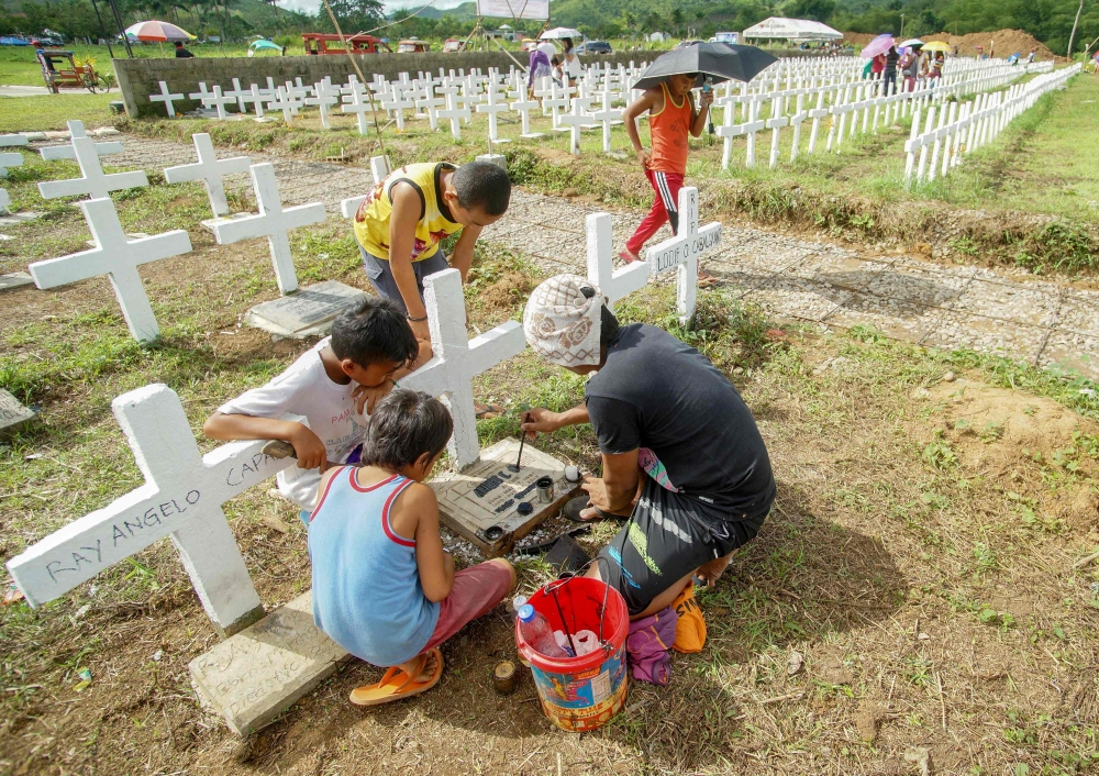 A family a tombstone of a relative at a mass grave for victims of Super Typhoon Haiyan during the fifth anniversary of the typhoon in Tacloban City, Leyte province, central Philippines on November 8, 2018.  AFP