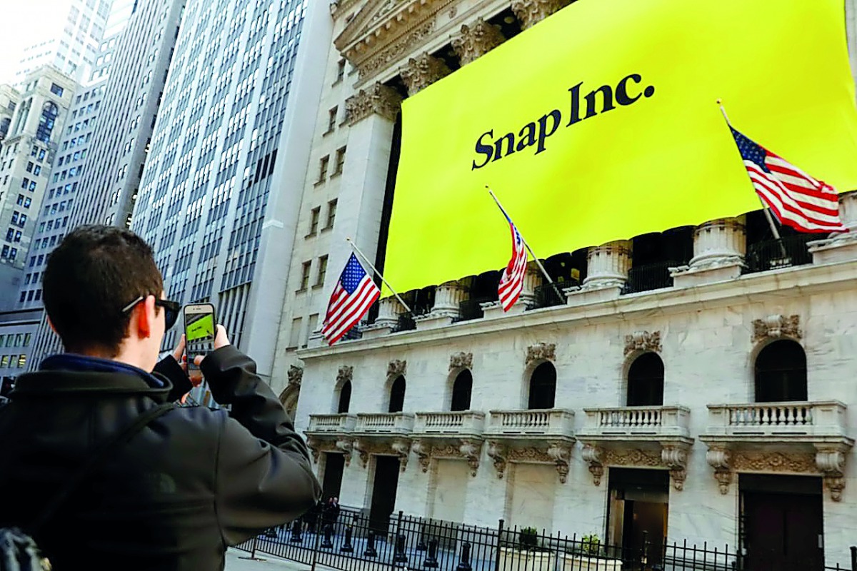 A man takes a photo of the New York Stock Exchange (NYSE) with a Snap Inc logo hung on the front of it.