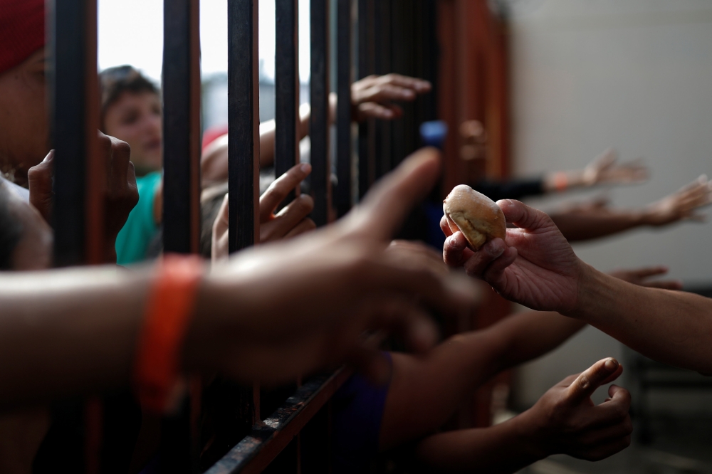 Migrants, part of a caravan traveling en route to the United States, try to get piece of bread in a shelter in Tijuana, Mexico November 17, 2018. Reuters/Carlos Garcia Rawlins