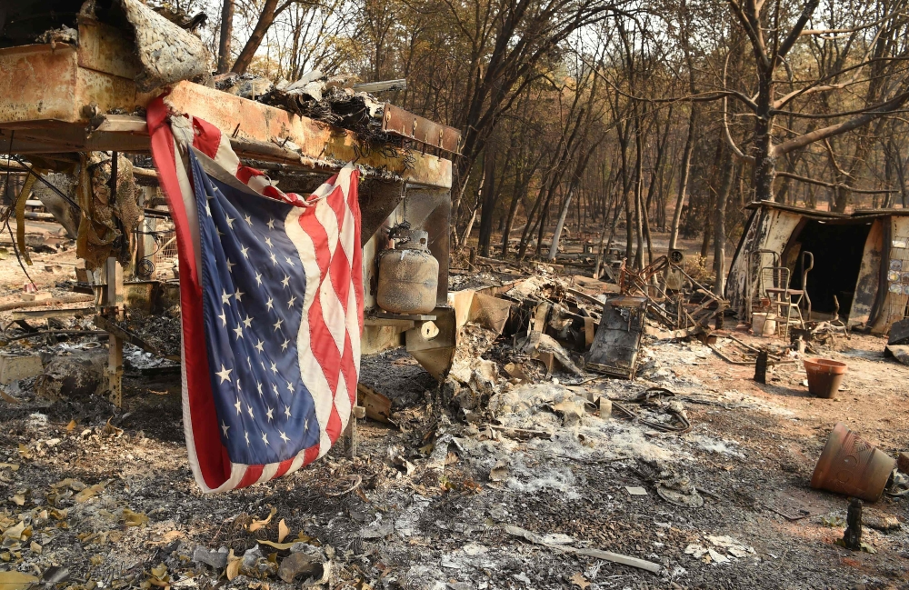 An American flag hangs at a burned out mobile home park in Paradise, California on November 18, 2018. The family lost a home in the same spot to a fire 10 years prior. / AFP / Josh Edelson 