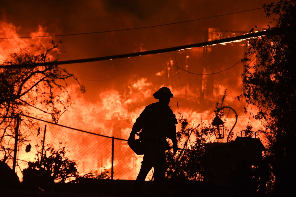 (FILES) In this file photo taken on November 9, 2018, a firefighter is silhouetted by a burning home along Pacific Coast Highway (Highway 1) during the Woolsey Fire in Malibu, California. AFP / Robyn Beck