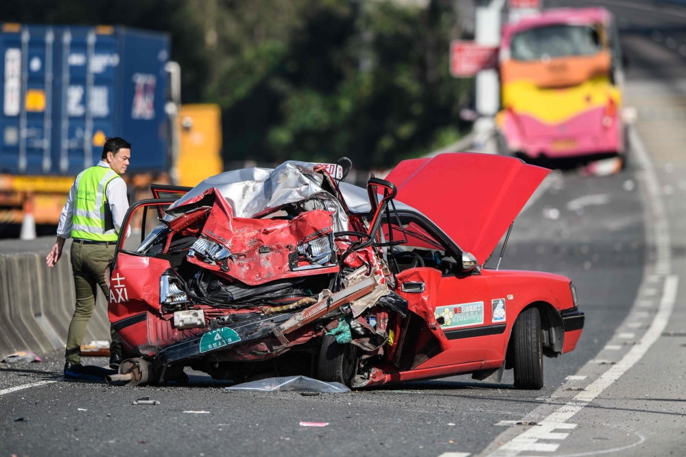 A policeman walks past a crushed taxi after a coach (back) collided with it in Hong Kong on November 30, 2018. / AFP / ANTHONY WALLACE 