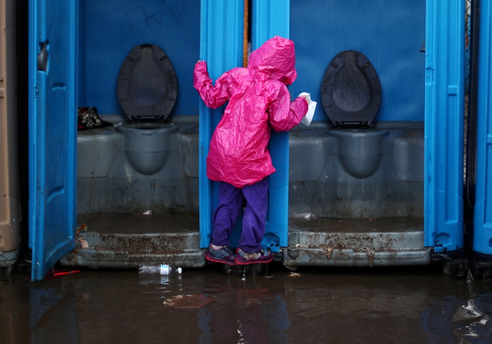 A migrant girl, part of a caravan of thousands from Central America trying to reach the United States, tries to avoid flooded ground by holding on to the door of a toilet after heavy rainfall in a temporary shelter in Tijuana, Mexico, November 29, 2018. R