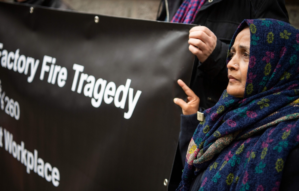 Saeeda Khatoon, mother of Aijaz Ahmed, who died in a fire in a Pakistani textile factory, and supporters of the civil trial against the textile discounter KiK, then the factory's main customer, hold a banner in front of the regional court in Dortmund on N