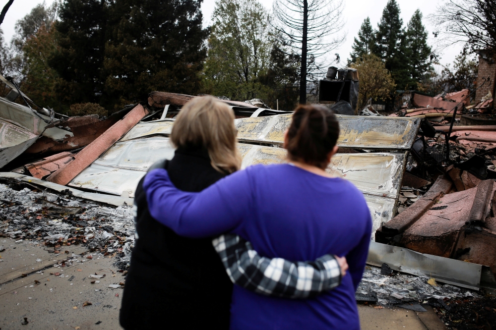 FILE PHOTO: Irma Corona (R) comforts neighbor Gerryann Wulbern in front of the remains of Wulbern's home after the two returned for the first time since the Camp Fire in Paradise, California, U.S. November 22, 2018. REUTERS/Elijah Nouvelage