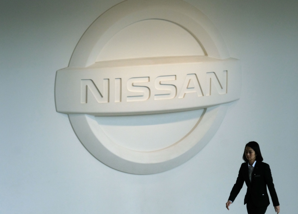 A woman walks under a Nissan logo at the company's headquarters in Yokohama on December 10, 2018. / AFP / Kazuhiro NOGI 
