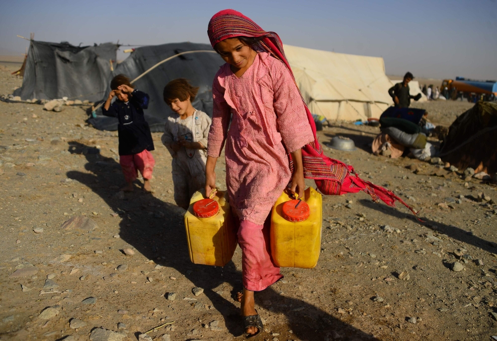 In this photo taken on August 3, 2018, a drought-displaced Afghan girl carries water containers filled from a tanker at a camp for internally displaced people in Injil district of Herat province. AFP / Hoshang Hashimi 