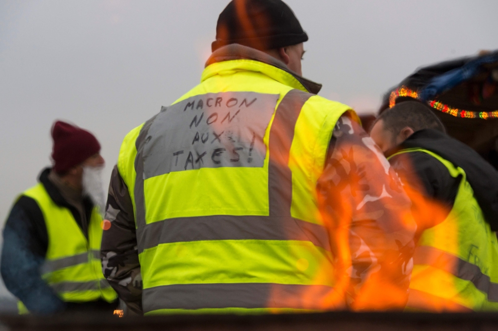 A protester wearing a yellow vest (gilet jaune) with a message reading 
