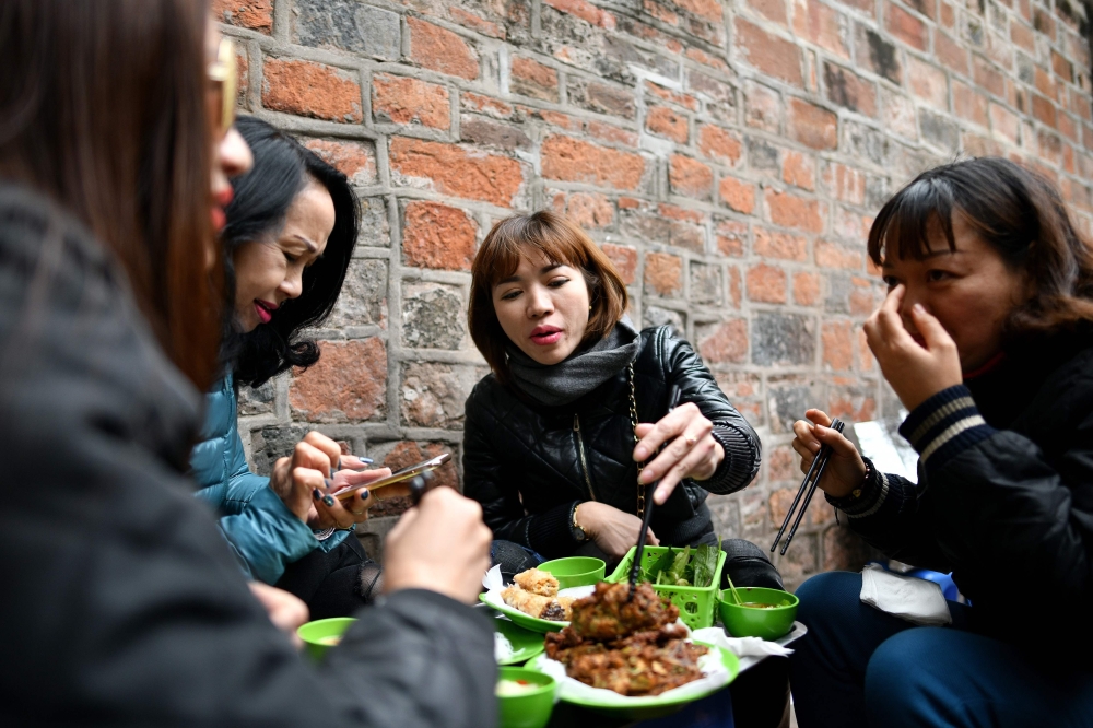This photograph taken on December 14, 2018 shows Vietnamese women eating 'cha ruoi' ragworms fritters at a street food stall in the old quarters of Hanoi. AFP / Manan Vatsyayana 