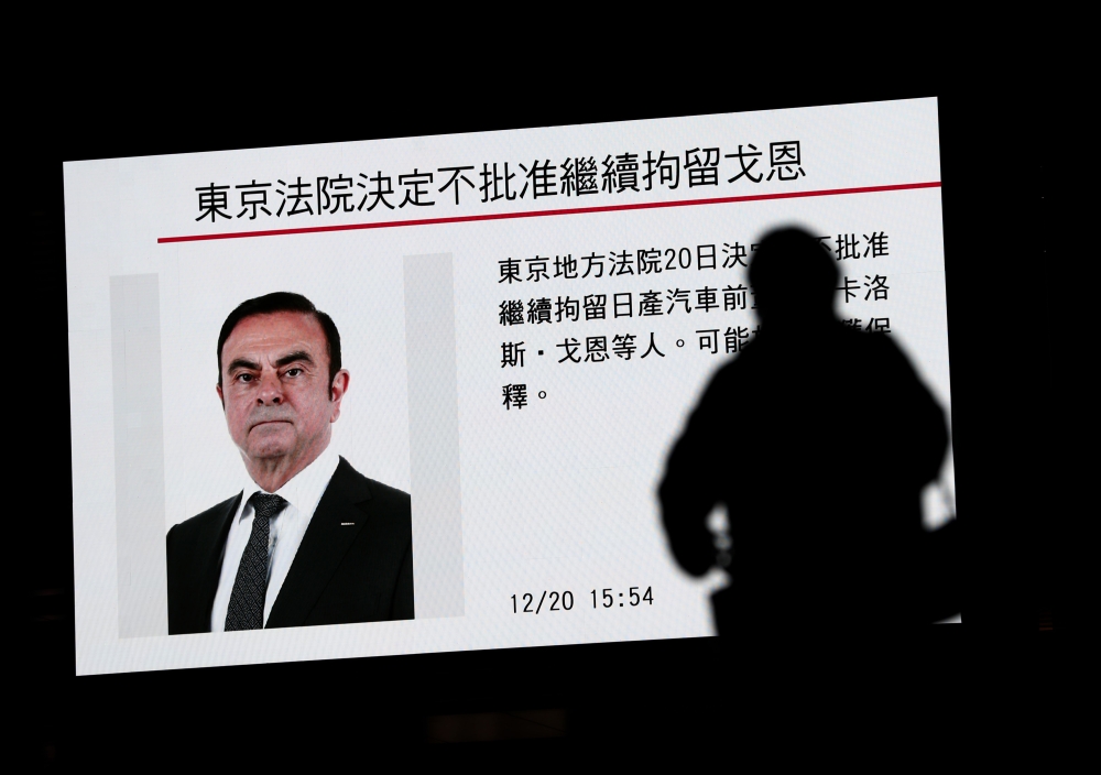A pedestrian walks past a television screen showing a news program featuring former Nissan chief Carlos Ghosn in Tokyo on December 20, 2018.  AFP / Behrouz MEHRI
