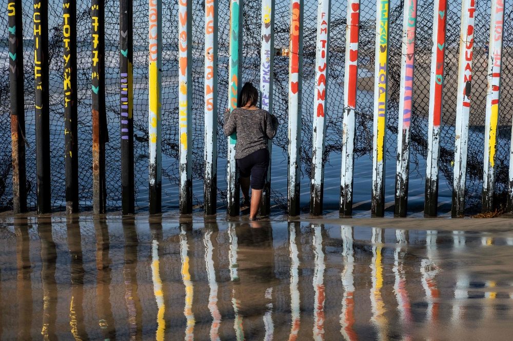 A girl from Salvador, part of the Central American migrants hoping to reach the United States, looks through the US-Mexico border fence in Playas de Tijuana, Baja California State, Mexico, on December 29, 2018.  AFP / GUILLERMO ARIAS
