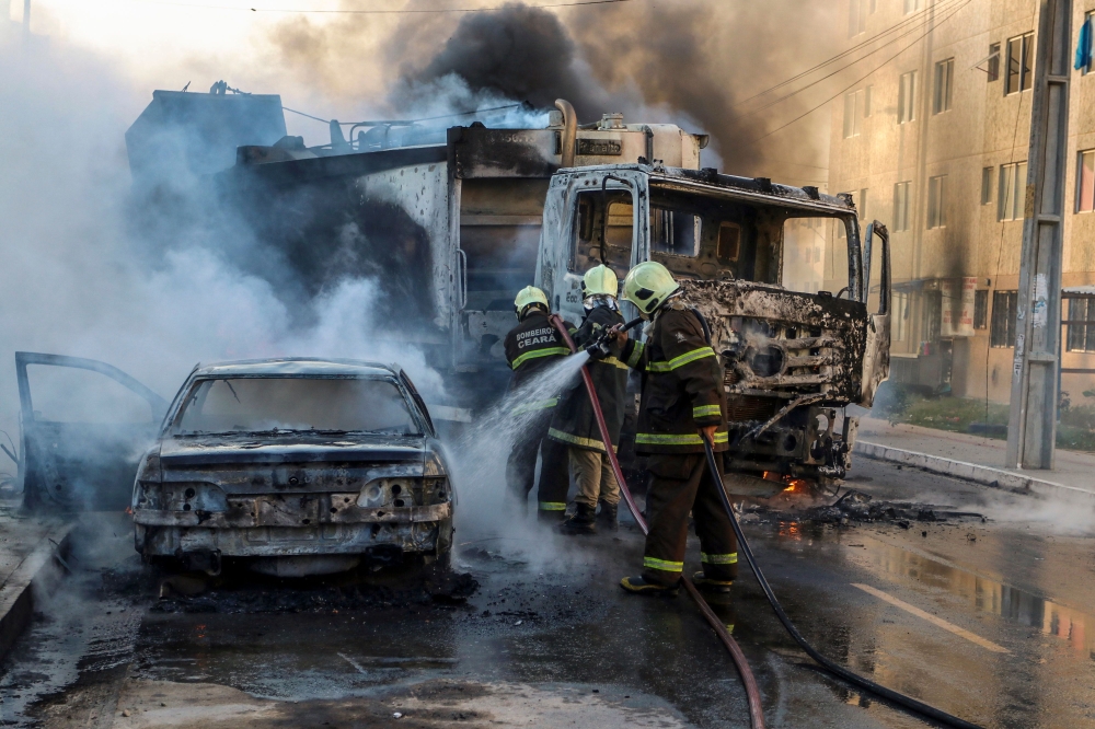 Firefighters putting out a burning truck and car during a wave of gang violence in Brazil's northeastern Ceara state, in the Conjunto Palmeiras neighborhood, city of Fortaleza, Ceara state, Brazil on January 3, 2019.  AFP PHOTO / O POVO / ALEX GOMES