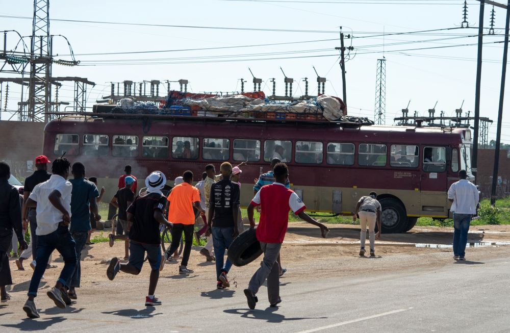 Protesters throw stones towards a bus which is alleged to be working during a 