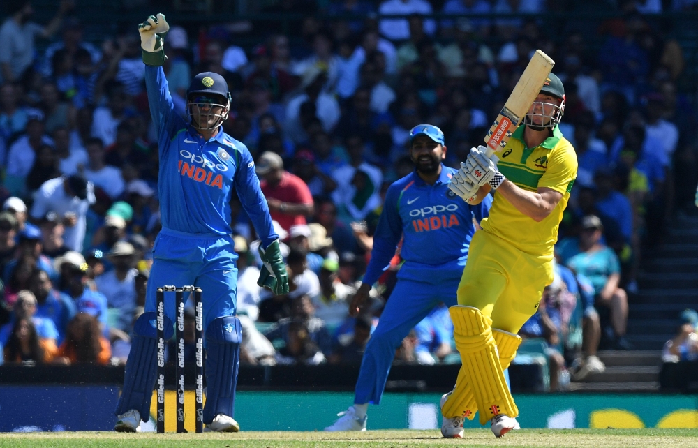 India's wicketkeeper Mahendra Singh Dhoni (L) shouts for a catch as Australia's batsman Shaun Marsh (C) plays a shot in the air during the first one-day International (ODI) match between Australia and India at the Sydney Cricket Ground in Sydney on Januar