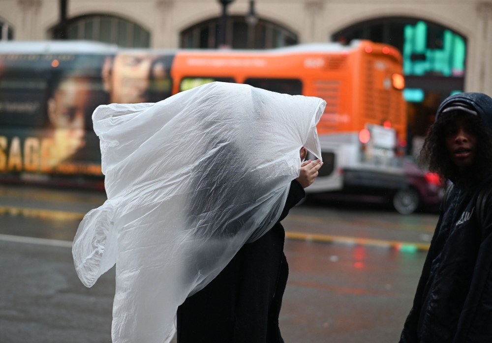 A woman covers her head with plastic as rain falls in Hollywood, California January 14, 2019. AFP / Robyn Beck